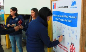 Funcionaria firma el compromiso con la Política de Seguridad del INH, con lápiz sobre un afiche en papel.