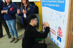 Funcionario firma el compromiso con la Política de Seguridad del INH, con lápiz sobre un afiche en papel.
