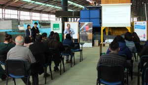 El Director Emilio Torres está de pie frente a los presentes, con un micrófono en la mano, hablando de la política de seguridad, mientras lo escuchan atentamente.