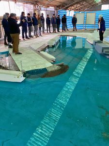 Jóvenes de pie, observan el modelo físico del Puerto San Antonio, con agua.