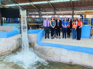 Mujeres de pie en el modelo físico embalse Ancoa, junto a una caída de agua.